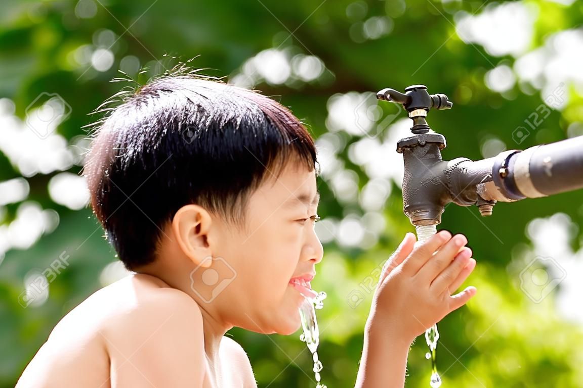 Close up jovem menino asiático tomar água de torneira velha e grunge no fundo bokeh verde. escassez de água e conceito do dia da terra.
