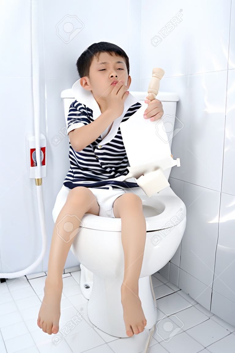 年輕的亞裔男孩坐在白色的廁所衛生間