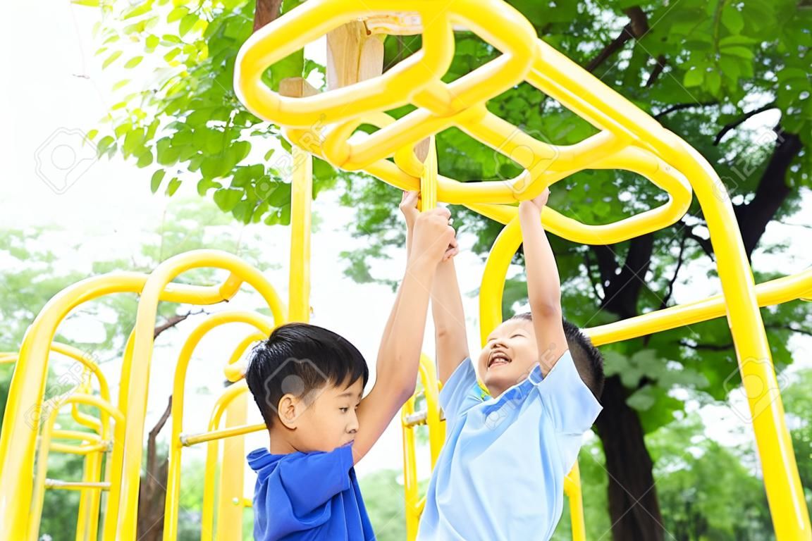 Jonge Aziatische jongen hangen de gele staaf aan zijn hand om te oefenen op de deur speeltuin onder de grote boom.