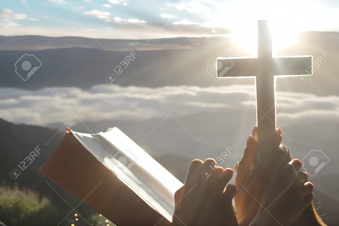 Christian woman praying on the mountain with morning sunrise. Hands crossed and Holy Bible . Background