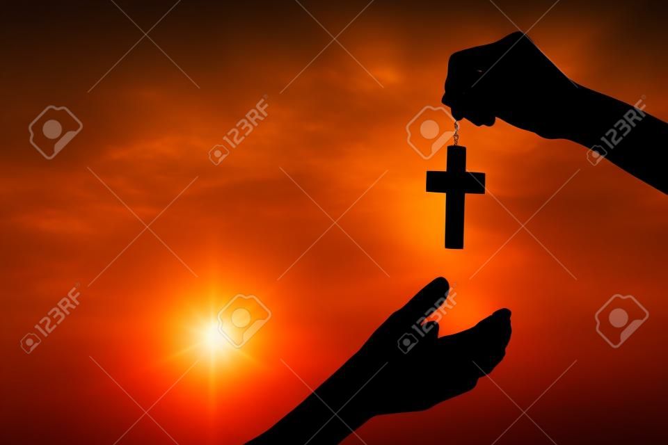 Silhouette des mains tenant une croix en bois sur fond de lever de soleil, Crucifix, symbole de la foi.