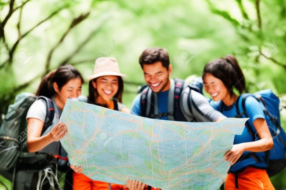 Hiking - hikers looking at map. Couple or friends navigating together smiling happy during camping travel hike outdoors in forest. Young mixed race Asian woman and man.