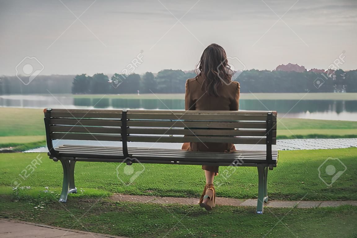 Joven y bella mujer con el pelo largo que se sienta en un banco en un parque de la ciudad