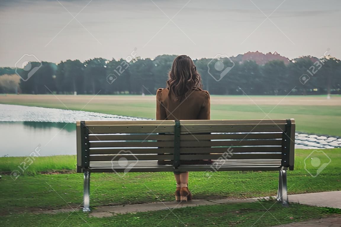 Piękna młoda kobieta z długimi włosami siedzi na ławce w parku miejskim