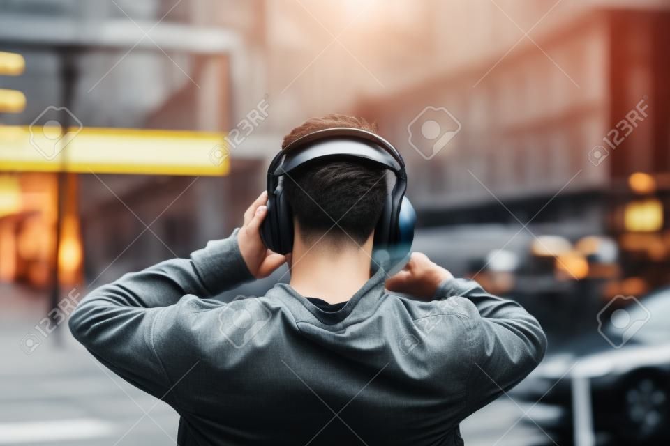 Widok z tyłu młodego człowieka ze słuchawkami słuchania muzyki na ulicach miasta