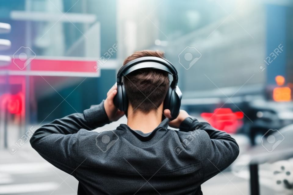 一个戴着耳机在城市街道上听音乐的年轻人的背影