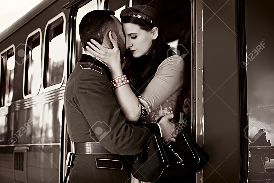 Vintage couple embracing on railway station platform as train is about to depart