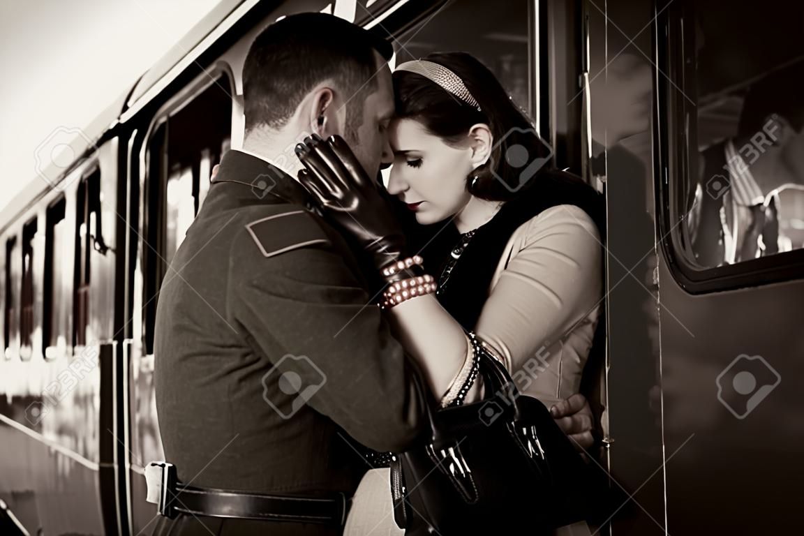 Vintage couple embracing on railway station platform as train is about to depart