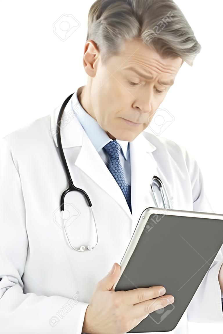 Confused mature male doctor looking at digital tablet isolated over white background
