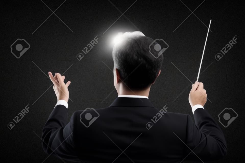 Vista traseira do maestro de música masculina dirigindo com seu bastão contra o fundo preto