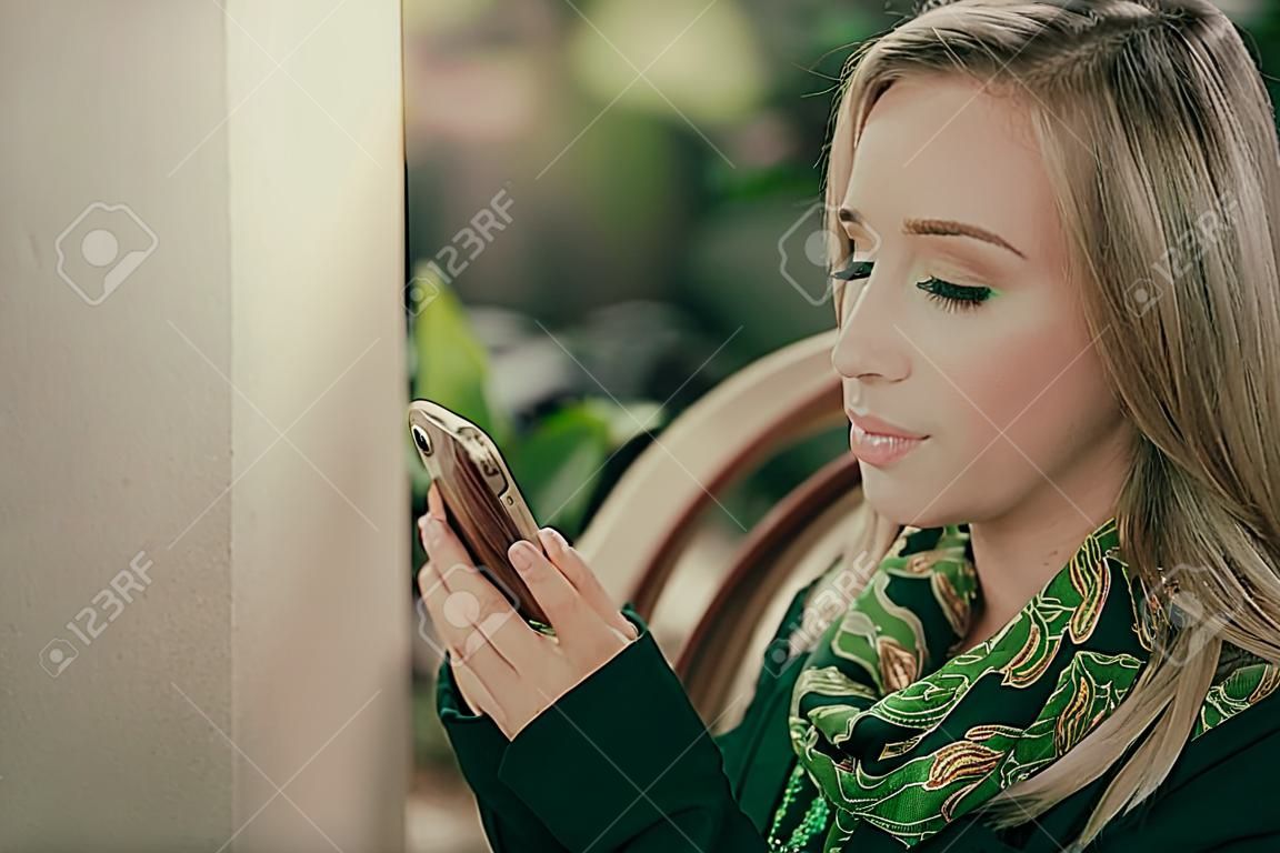 Mujer joven tomando café y usando su teléfono en la cafetería.