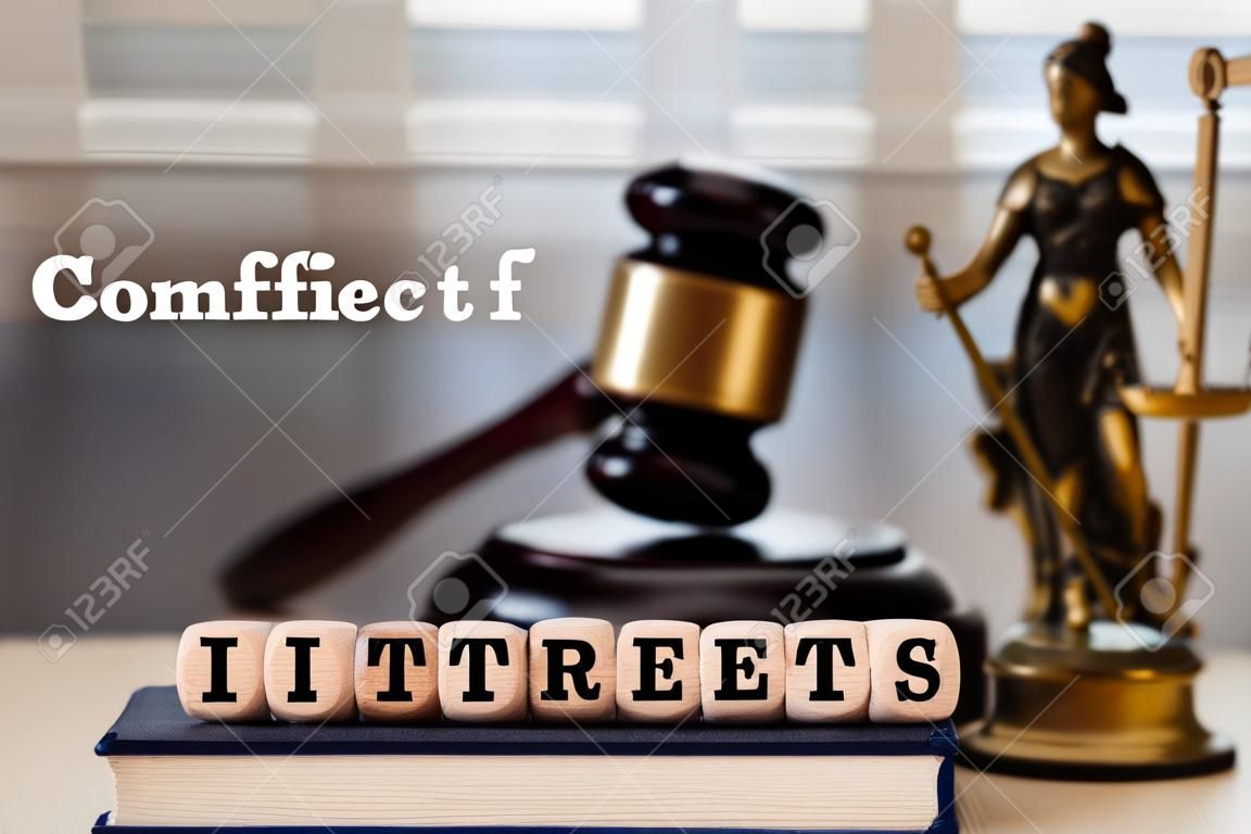 Words CONFLICT OF INTERESTS composed of wooden dices. Wooden gavel and statue of Themis in the background. Closeup