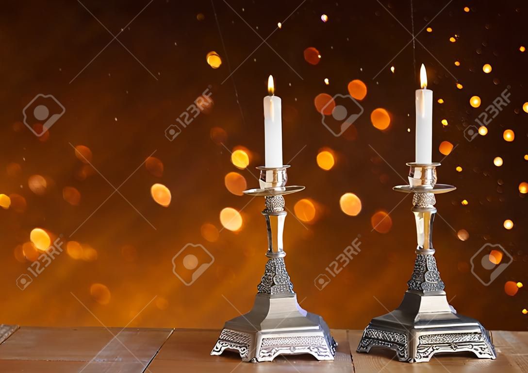 dos candelabros con velas encendidas sobre la mesa de madera y fondo del brillo de la vendimia