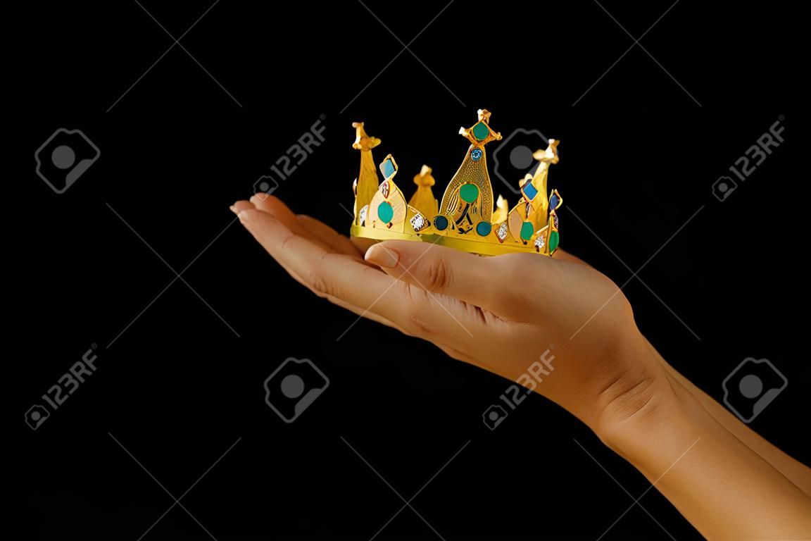 Mano de mujer sosteniendo una corona para mostrar la victoria o ganar el primer lugar sobre fondo negro