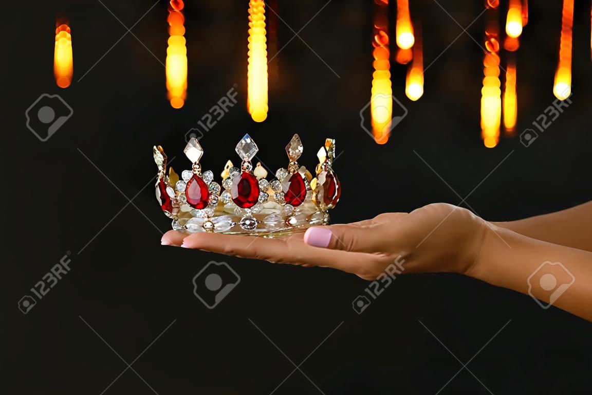 Mão de uma mulher segurando uma coroa para mostrar a vitória ou ganhar o primeiro lugar sobre fundo preto com sobreposição de brilho
