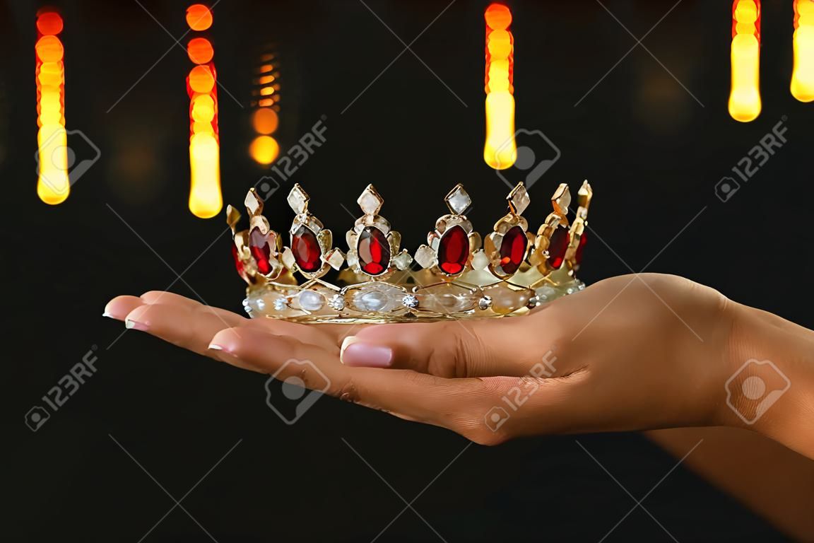 Main de femme tenant une couronne pour la victoire du spectacle ou gagnant la première place sur fond noir avec superposition de paillettes