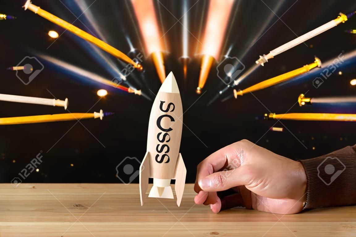 man's hand holding wooden rocket with word - success - over glitter black background