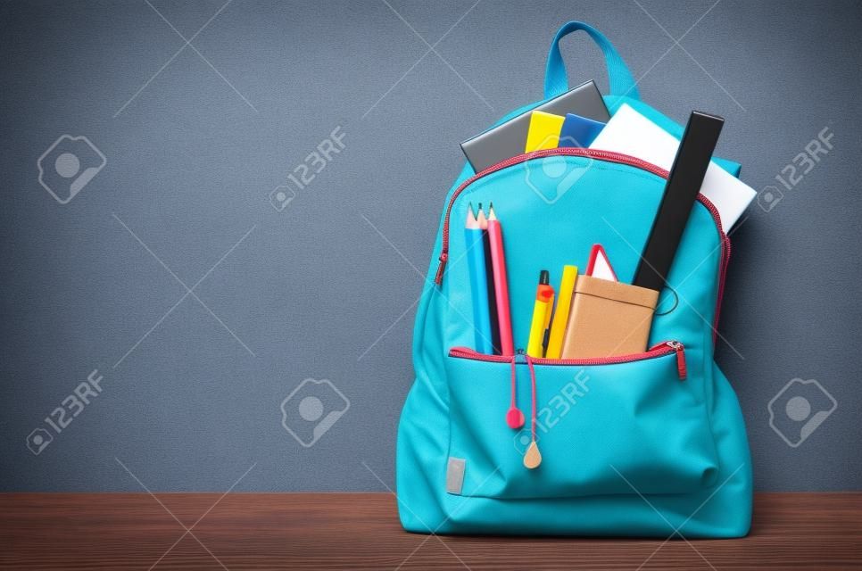saco da escola com artigos de papelaria e cadernos na frente do fundo azul de madeira.