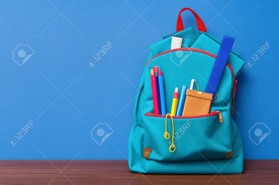 school bag with stationery and notebooks in front of wooden blue background. Back to school concept