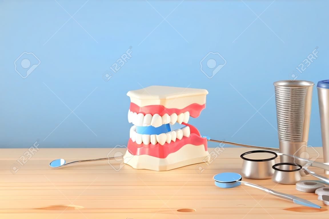 Uso de herramientas de cuidado dental para dentista y modelo de dientes de plástico en la clínica. Fondo azul de madera