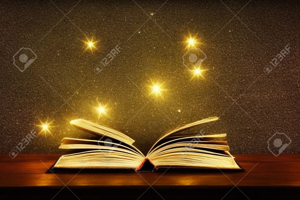 Imagen mágica de un libro antiguo abierto sobre una mesa de madera con una capa brillante