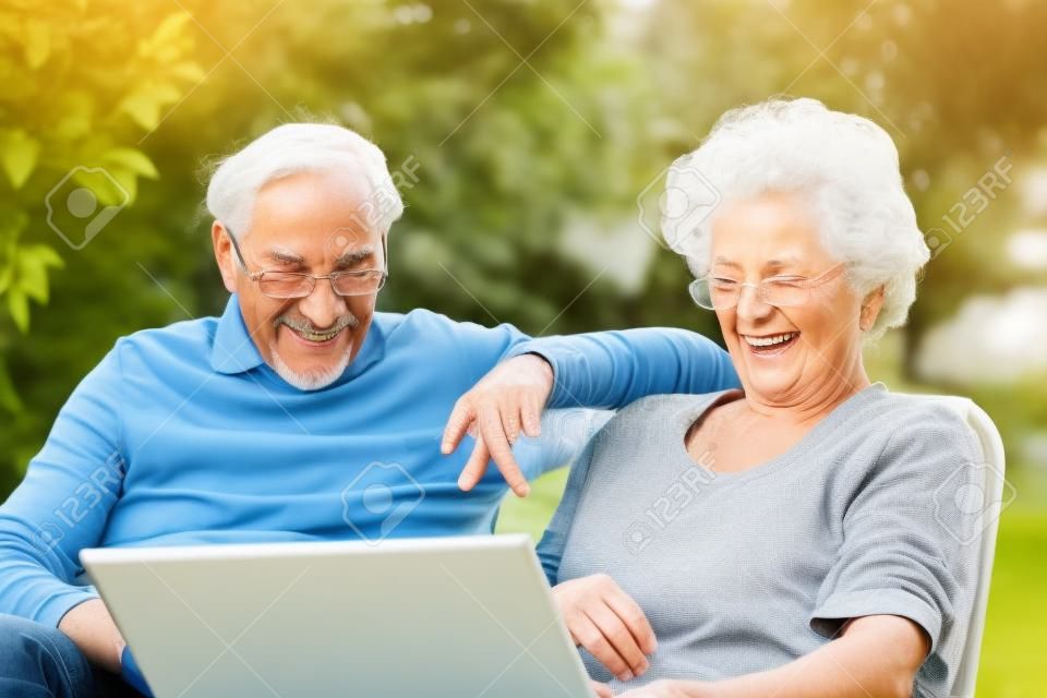 Una coppia di anziani si diverte con il portatile nel giardino esterno.