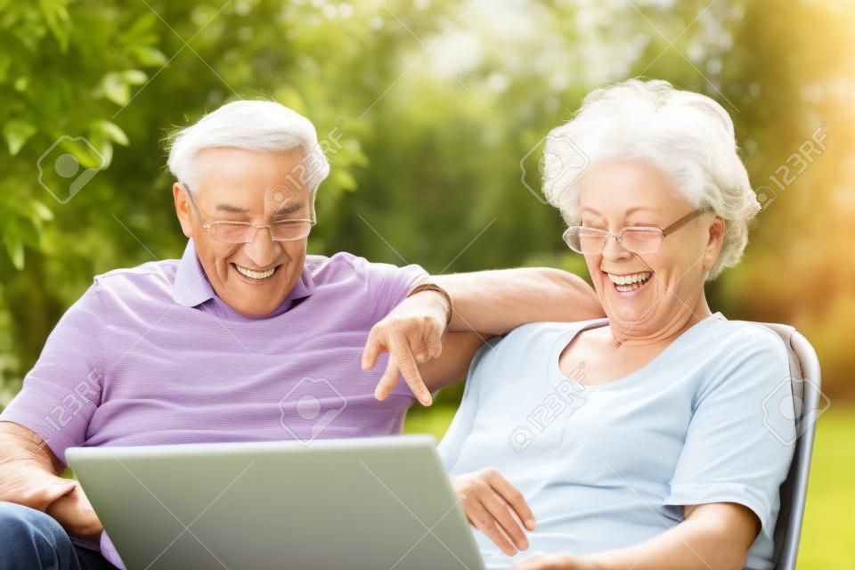 Una coppia di anziani si diverte con il portatile nel giardino esterno.