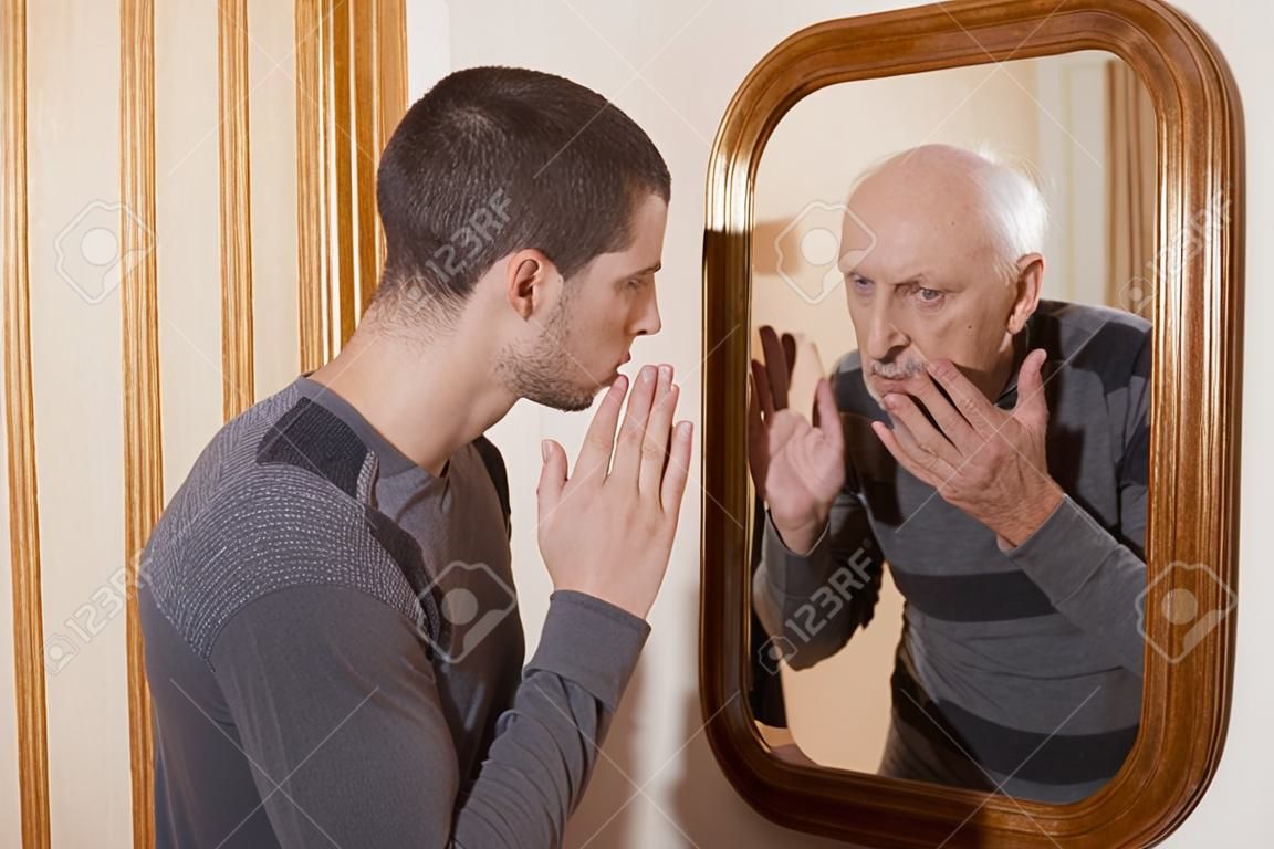 年輕人看著一個老鏡子中的自己