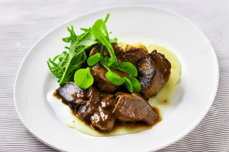 Cooked veal cheeks in gravy with potatoes and cabbage, decorated fresh herbs in white plate. Close-up
