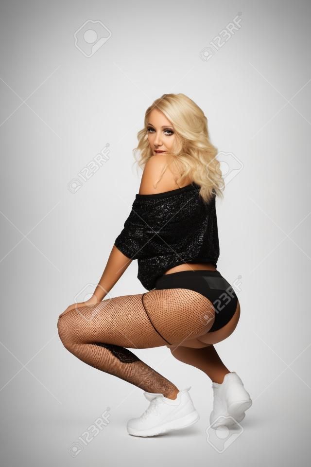beautiful blonde girl in booty shorts and fishnet dancing twerk isolated on white background