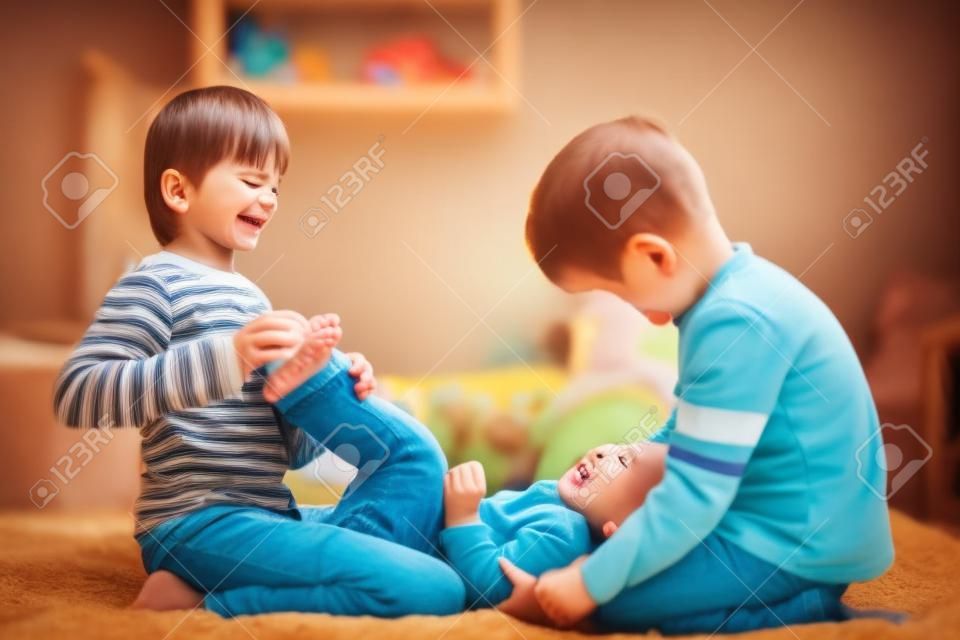 Dzieci, bracia, bawiące się w domu, łaskoczące stopy śmiejące się i uśmiechnięte
