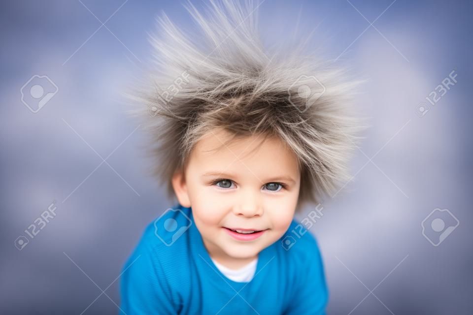 Menino bonito com cabelo elétrico estático, tendo seu retrato engraçado levado ao ar livre em um trampolim