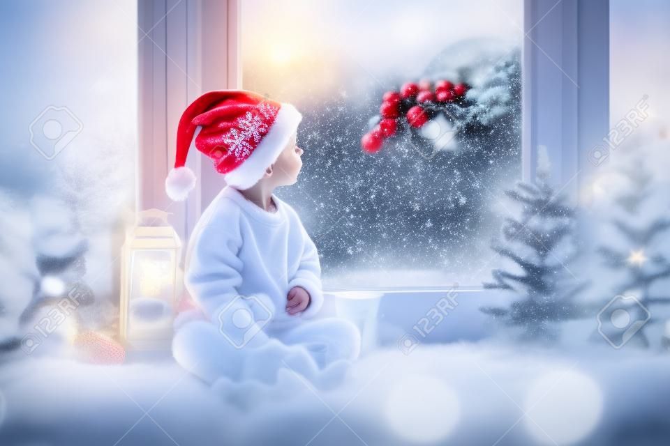 Schattig kind, zittend op een raam, op zoek naar de kerstman, kerstversiering op het raam