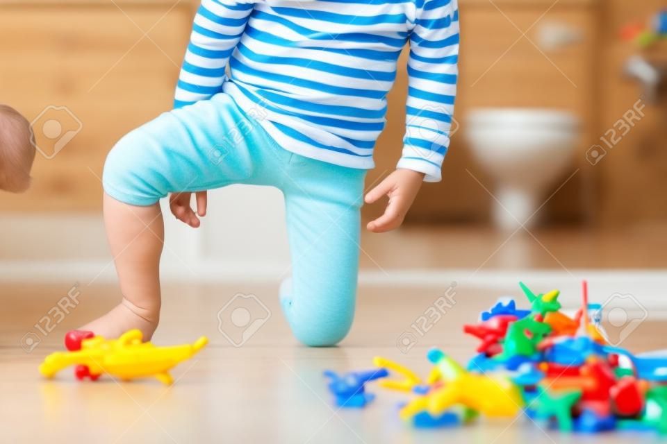 Małe dziecko, chłopiec, sika w spodnie podczas zabawy zabawkami, dziecko jest rozproszone i zapomina iść do toalety w domu