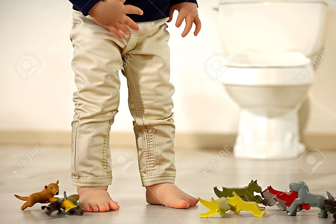 Bambino piccolo, ragazzo, pipì nei pantaloni mentre gioca con i giocattoli, bambino distratto e dimentica di andare in bagno a casa