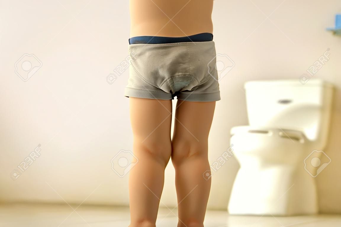 Niño pequeño, niño, se orina en los pantalones mientras juega con juguetes, niño distraído y se olvida de ir al baño en casa