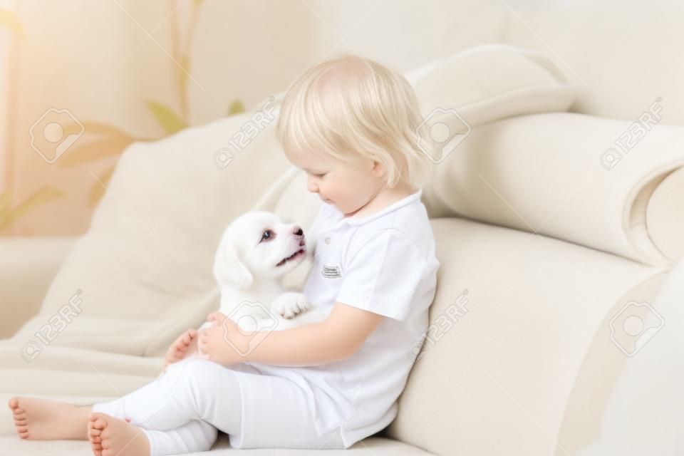 Schattig klein blond kind, peuter jongen, spelen met witte puppy maltese hond thuis