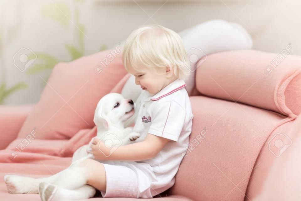 Schattig klein blond kind, peuter jongen, spelen met witte puppy maltese hond thuis