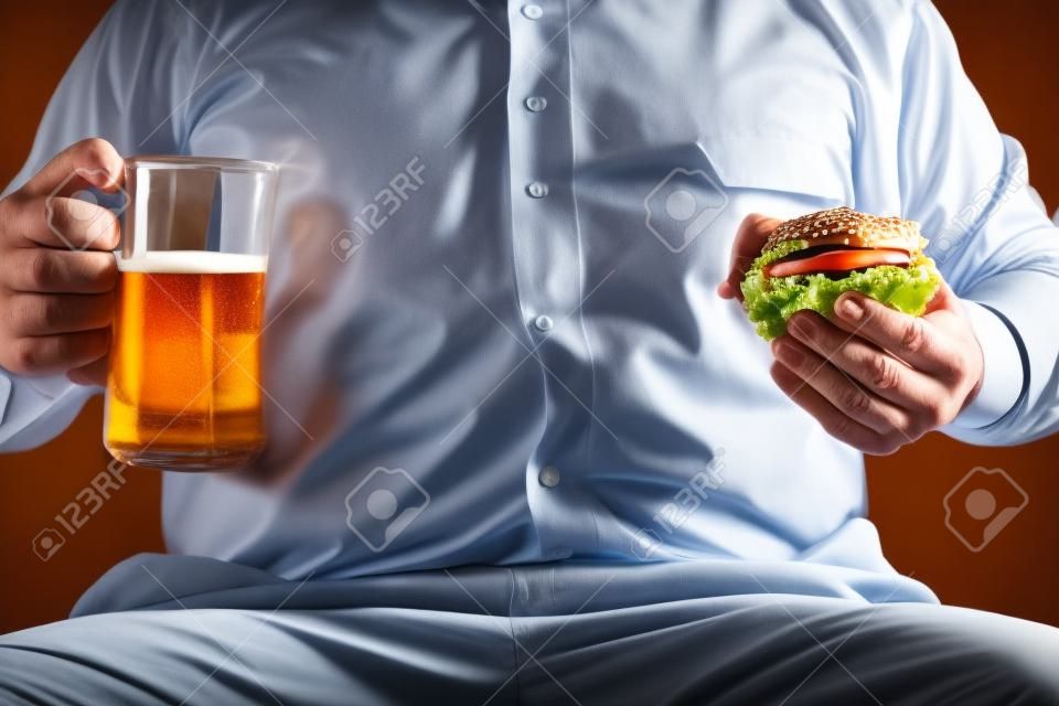 胖商人拿着啤酒杯和汉堡包