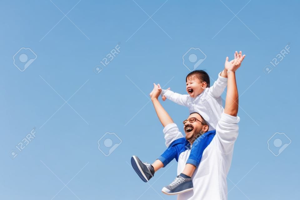 gelukkig vader draagt zijn dochter op schouders met blauwe lucht achtergrond