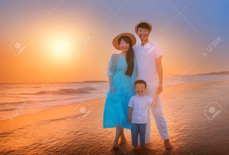 Szczęśliwa azjatycka rodzina stojąca na plaży o zachodzie słońca
