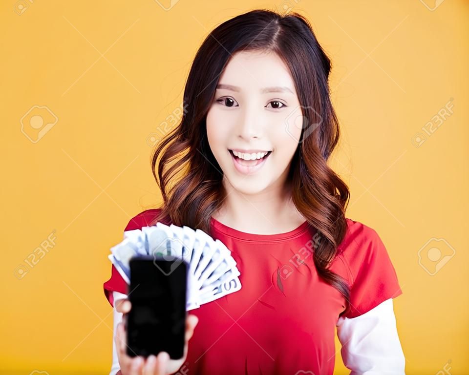 携帯電話とお金を持っている幸せな若い女性。
