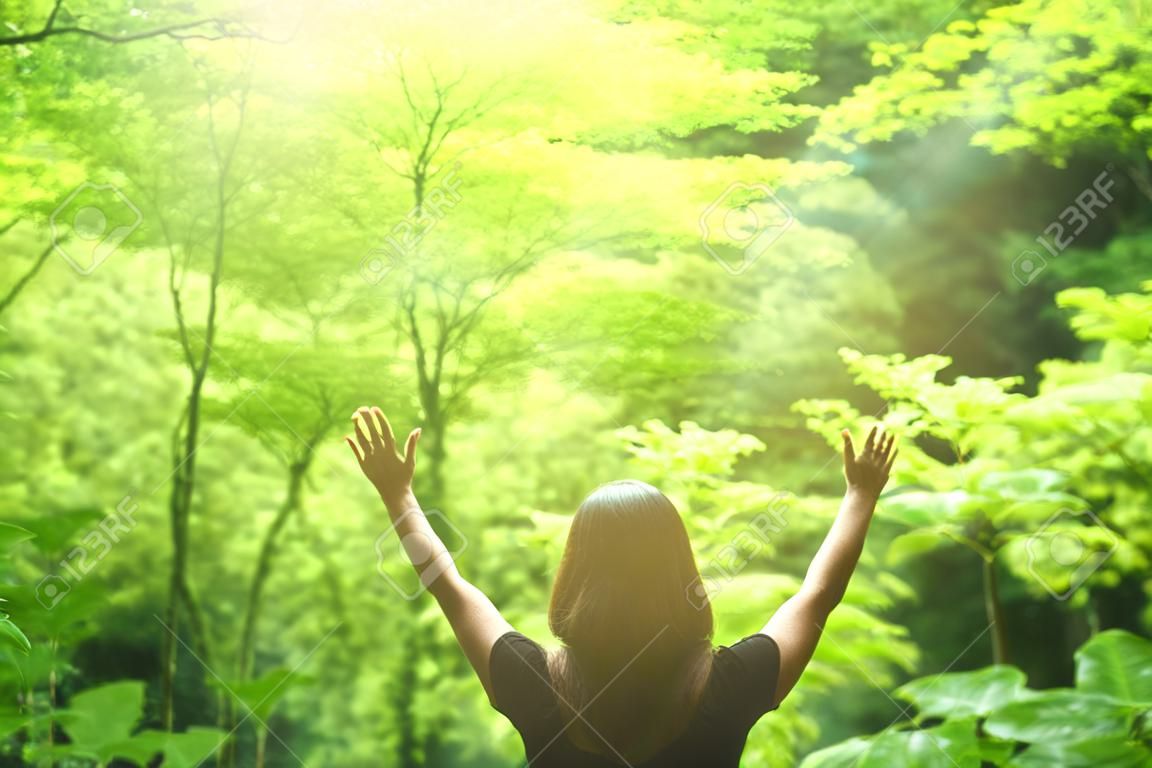 Freedom feel good and travel adventure concept. Copy space silhouette woman rising hands in nature green leaf background in forest. Vintage tone filter effect color style.