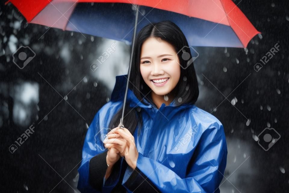 Giornata di pioggia donna asiatica che indossa un impermeabile all'aperto. Lei è felice.