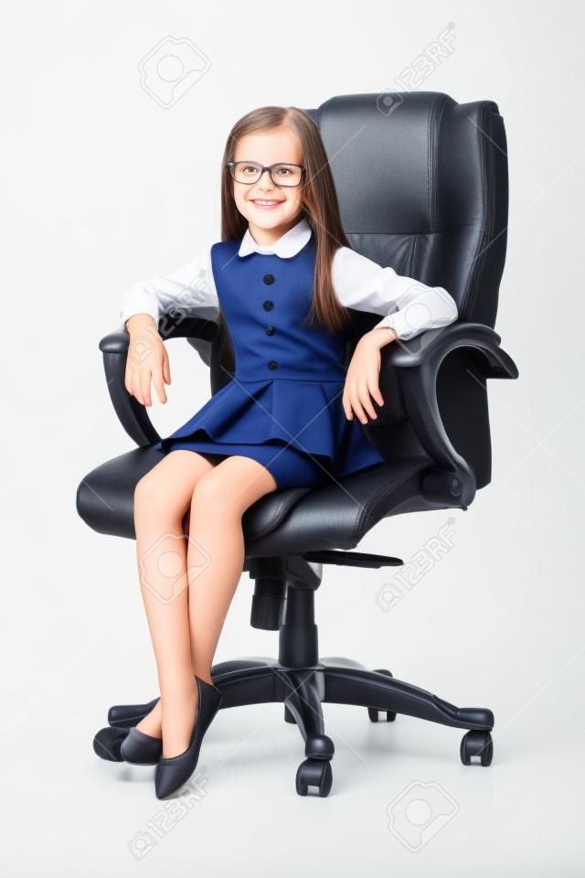 Adorable niña sonriente linda que se sienta en la silla en la oficina vestida como una empresaria en el fondo blanco morena caucásica hermoso atractivo feliz exitoso confiado aislado administrar.