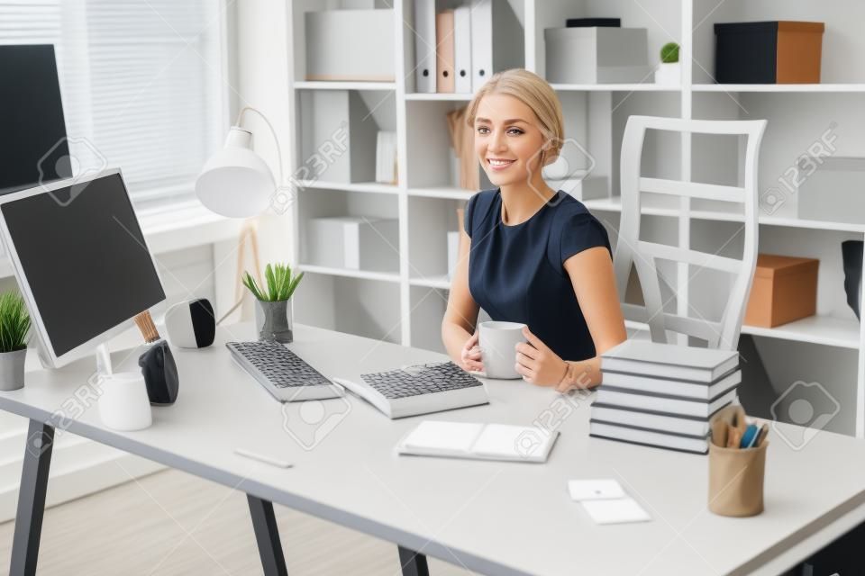 Uma bela menina loira jovem em uma blusa cinza está trabalhando no escritório. foto com profundidade de campo