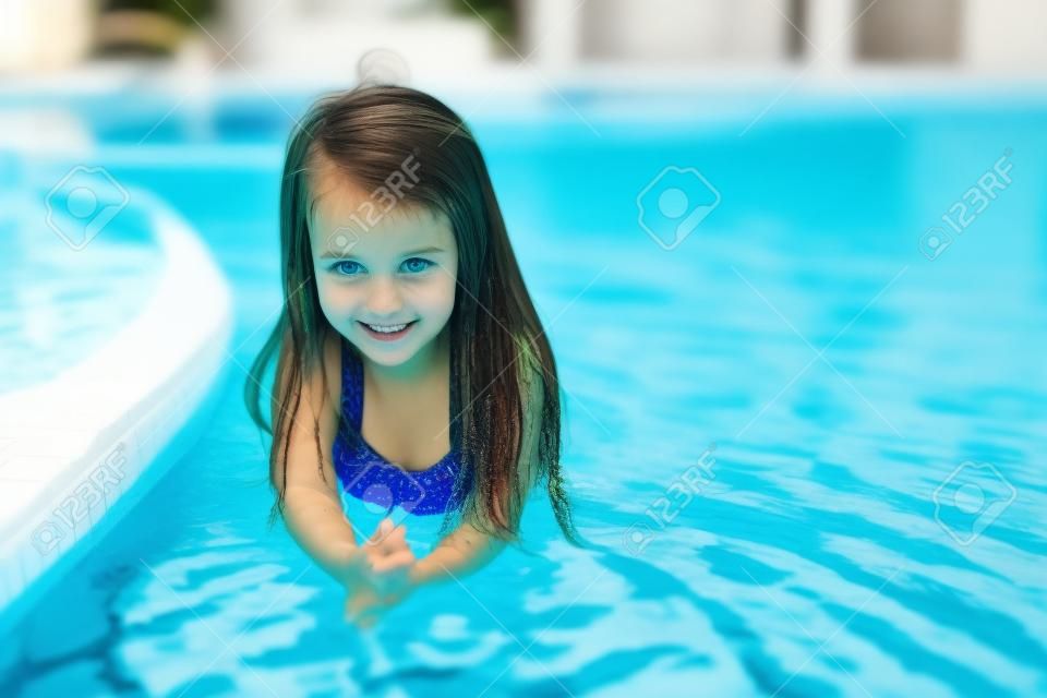 Adorable girl in the swimming pool looks at camera