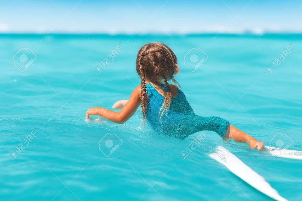 Niña linda que nadan en una tabla de surf en el mar turquesa