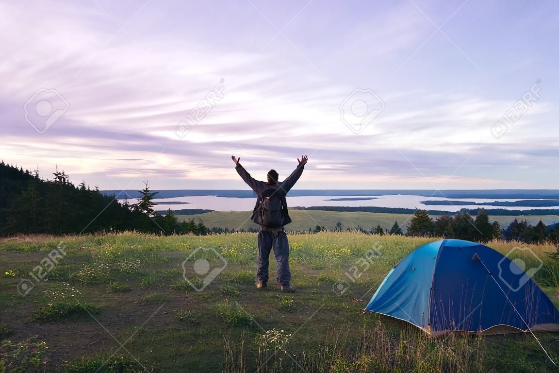 Hiker meets good morning with raised hands just got out from his tent.