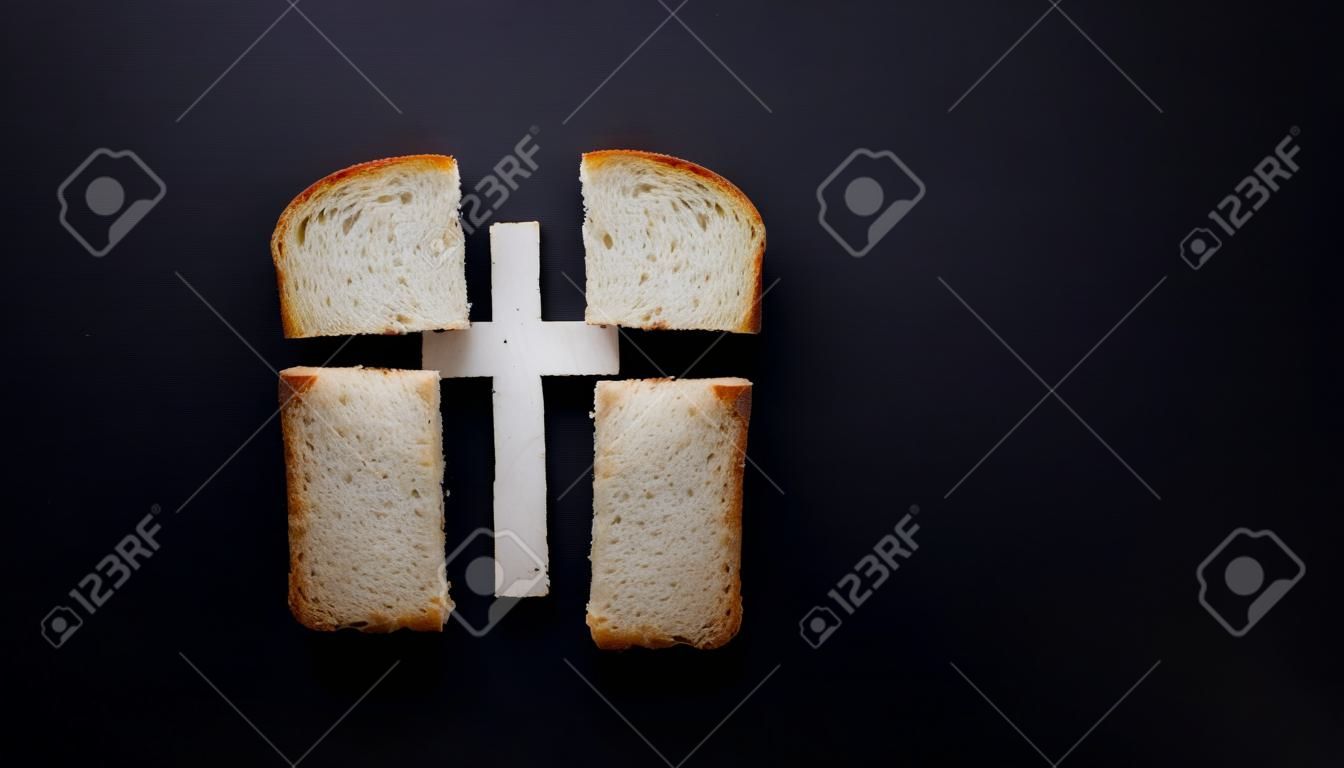 Nuestro pan de cada día, metáfora y signo. Cruz, valores cristianos, concepto de religión cristiana. Pan en forma de cruz sobre un fondo negro, vista superior con espacio de copia